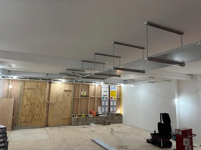 Cable tray and lighting installed across the ceiling of a commercial unit during fit-out, with partition walls under construction