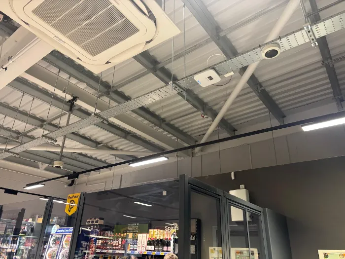 Ceiling cassette air conditioning unit beside cable containment and lighting in a retail store